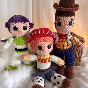 May include: Three handmade crochet dolls inspired by characters from the animated film Toy Story. The dolls include Buzz Lightyear in green and white, Jessie in red and yellow, and Woody in brown and blue. Each doll has large, expressive eyes.