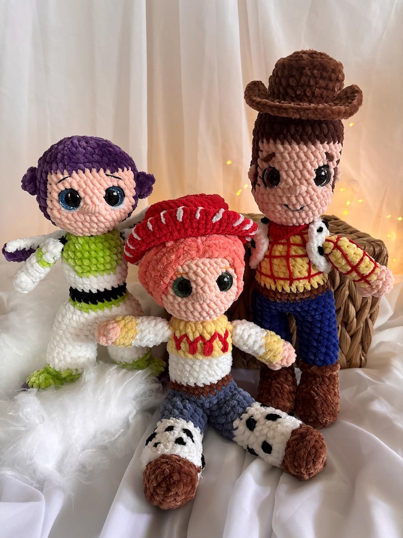 May include: Three handmade crochet dolls inspired by characters from the animated film Toy Story. The dolls include Buzz Lightyear in green and white, Jessie in red and yellow, and Woody in brown and blue. Each doll has large, expressive eyes.