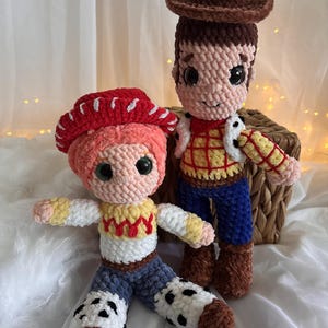 May include: Two handmade crochet dolls, one with a brown cowboy hat and the other with a red cowgirl hat. The dolls have detailed features, including facial expressions and clothing, and are set against a soft, neutral background.