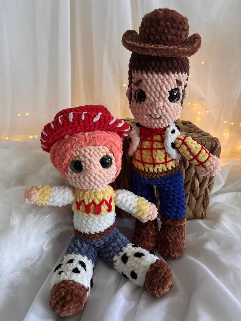 May include: Two handmade crochet dolls, one with a brown cowboy hat and the other with a red cowgirl hat. The dolls have detailed features, including facial expressions and clothing, and are set against a soft, neutral background.