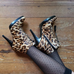 May include: A pair of leopard print heeled boots with black laces and tassels. The boots are worn with black fishnet stockings with a diamond pattern.