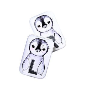Pode incluir: Dois ímanes retangulares brancos com uma ilustração em aquarela de um pinguim. O pinguim é preto e branco com uma expressão fofa. Um íman tem a letra "L".