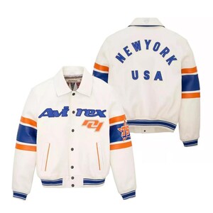May include: White jacket with blue and orange accents. The jacket features the text "Avi-rex" on the front and "NEW YORK USA" on the back. The sleeves have blue and orange stripes, and the jacket has a button-up front.