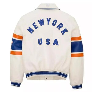 May include: Cream-colored jacket with blue and orange accents. The back features the text "NEW YORK USA" in blue lettering. The sleeves have blue and orange stripes. The jacket has a collar and a blue and white striped hem.