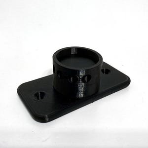 May include: A black 3D-printed object with a cylindrical part on a rectangular base. The cylinder has circular cutouts. The base has two holes. The object is on a white background. Measurements are in cm.