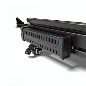 Puede incluir: Un concentrador USB negro con múltiples puertos e indicadores azules. El concentrador está montado en un marco negro con ruedas, diseñado para la movilidad. Los puertos están dispuestos en fila, lo que sugiere un enfoque en la conectividad y la transferencia de datos.