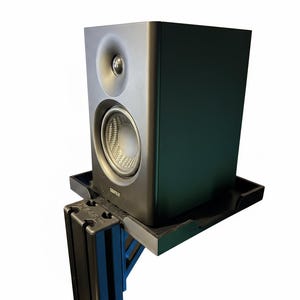 Op de afbeelding: Een zwarte luidspreker met een zilveren tweeter en woofer, gemonteerd op een zwarte plank. De luidspreker is rechthoekig met afgeronde hoeken en staat op een zwarte beugel. Ontworpen voor audio.