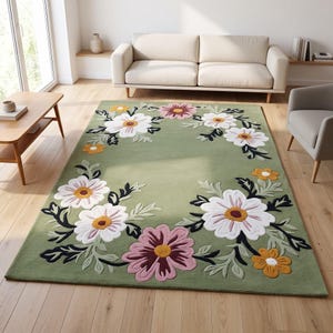 May include: A rectangular area rug featuring a sage green background with a floral pattern. The design includes large white, pink, and yellow flowers with dark green and light green leaves arranged in a border around the center of the rug.