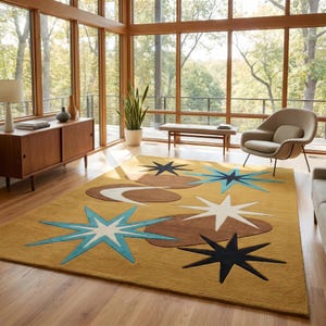 May include: A rectangular area rug featuring a mustard yellow background with a pattern of brown organic shapes, white starbursts, and light blue and dark navy blue starbursts. The rug has a textured pile and covers a wooden floor surface.