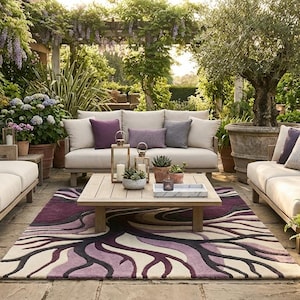 Può includere: Set da patio esterno con divani beige, cuscini viola e un tavolino in legno. Un tappeto fantasia con vortici viola e bianchi è al centro. La scena è circondata da una vegetazione lussureggiante e piante in vaso.