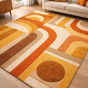 May include: A large, rectangular rug with a retro design. The rug features a geometric pattern of curved lines and shapes in shades of orange, yellow, brown, and beige. The rug is made of a soft, plush material.