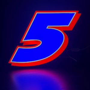 May include: A neon sign in the shape of the number 5. The number is blue with a red outline and a thin yellow border. The sign is illuminated against a dark blue background, with a reflection below.