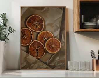 May include: A framed print featuring five dried orange slices arranged on crumpled brown paper. The oranges are a warm brown color, with visible segments and a central star-shaped pattern. The frame is a light brown color.