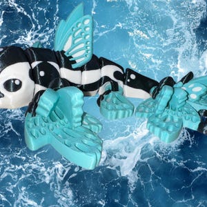May include: A whimsical, articulated creature with a black and white body, a light blue horn, and light blue wings and fins. The creature is set against a backdrop of blue water, suggesting an aquatic theme. The design incorporates butterfly-like wings.