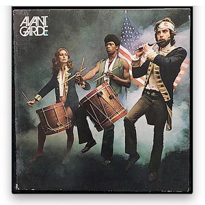 May include: Album cover for "Avant Garde" featuring three figures in colonial-era attire. One plays a flute, while the others play drums. The American flag is in the background. The album title is in the upper left corner.