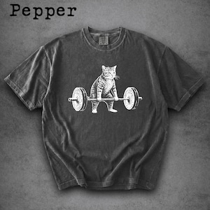 Könnte beinhalten: Dunkelgraues T-Shirt mit weißer Grafik einer Katze beim Gewichtheben. Das Wort "Pepper" ist oben links aufgedruckt. Das Shirt hat einen Rundhalsausschnitt und kurze Ärmel. Ein lässiges T-Shirt für Katzenliebhaber.