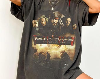 Könnte beinhalten: Dunkelgraues T-Shirt mit einem Filmplakat-Design für "Pirates of the Caribbean: Am Ende der Welt". Die Grafik zeigt Charaktere und den Filmtitel in Rot und Weiß. Das T-Shirt hat einen Vintage-Look.