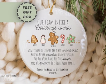 May include: White ceramic Christmas ornament with gold string, featuring a festive design. The ornament reads "OUR TEAM IS LIKE A Christmas cookie" with cookie illustrations and text. The text includes "Thanks for Being the Best Team Ever - 2025".