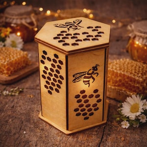 Può includere: Una lanterna esagonale in legno con intagli a forma di api e favi. La lanterna presenta una silhouette di ape sul lato e sulla parte superiore, con motivi a favo. La luce calda all'interno illumina gli intagli, creando un'atmosfera accogliente.