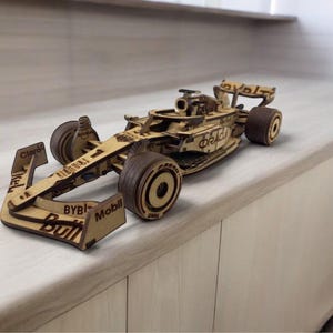 Op de afbeelding: Een houten model van een Formule 1-raceauto. De auto is gemaakt van lichtbruin hout met donkerbruine wielen en accenten. Sponsorlogo's zoals "BYBIT", "Mobil" en "Oracle" zijn zichtbaar op de carrosserie.