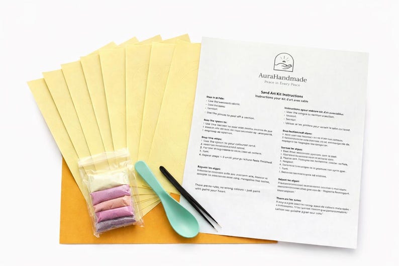 May include: Sand art kit with instructions. Includes yellow paper sheets, a bag of colored sand, a teal spoon, and a black tool. The instructions are printed on a white sheet with the Aura Handmade logo.