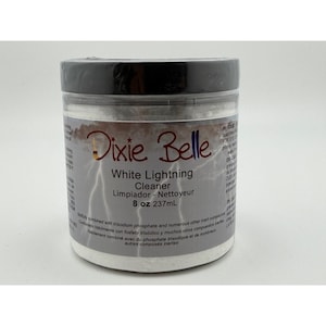 May include: A clear plastic jar with a black lid, labeled "Dixie Belle White Lightning Cleaner." The label includes the text "8 oz 237mL" and a lightning bolt graphic. The jar contains a white powder.