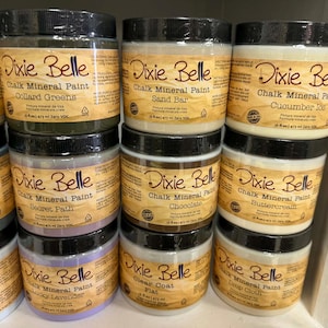May include: A collection of Dixie Belle Chalk Mineral Paint jars in various colors including Collard Greens, Sand Bar, Cucumber Ice, Secret Path, Chocolate, Buttercream, Lucky Lavender, Clear Coat Flat, and Drop Cloth, each 16 fl oz.
