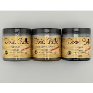 May include: Three clear plastic jars of Dixie Belle glaze with black lids. The labels read Grunge Glaze, Van Dyke Brown Glaze, and Black Glaze. Each jar contains 8 fl oz of product and features a red New Formula sticker on the tan-colored label.