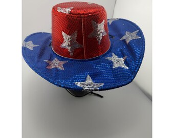 May include: A sequined cowboy hat featuring a red cylindrical crown and a wide blue brim. The hat is decorated with silver sequin star patterns distributed across both the red crown and the blue brim, creating a patriotic color scheme.