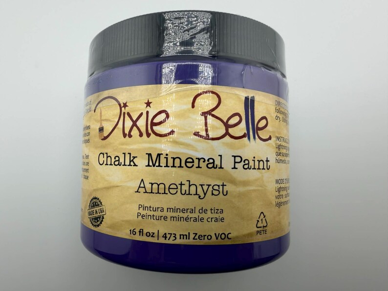 May include: A 16 fl oz jar of Dixie Belle Chalk Mineral Paint in the color Amethyst. The jar features a black lid, a tan label with dark brown text, and the product name clearly printed on the front. The label also indicates Zero VOC.
