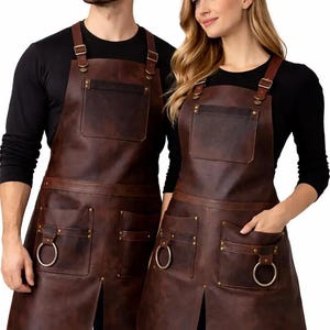 May include: Brown leather aprons with multiple pockets, metal ring accents, and adjustable straps. The aprons have a classic design, suitable for various uses. The aprons are worn by two people, one male and one female.