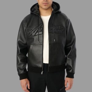 May include: Black leather hooded jacket with a zip-up front, featuring the embossed text "Aries" on the chest. The jacket has a ribbed hem and cuffs, and a kangaroo pocket. The model is wearing a white t-shirt underneath.