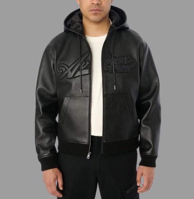 May include: Black leather hooded jacket with a zip-up front, featuring the embossed text "Aries" on the chest. The jacket has a ribbed hem and cuffs, and a kangaroo pocket. The model is wearing a white t-shirt underneath.