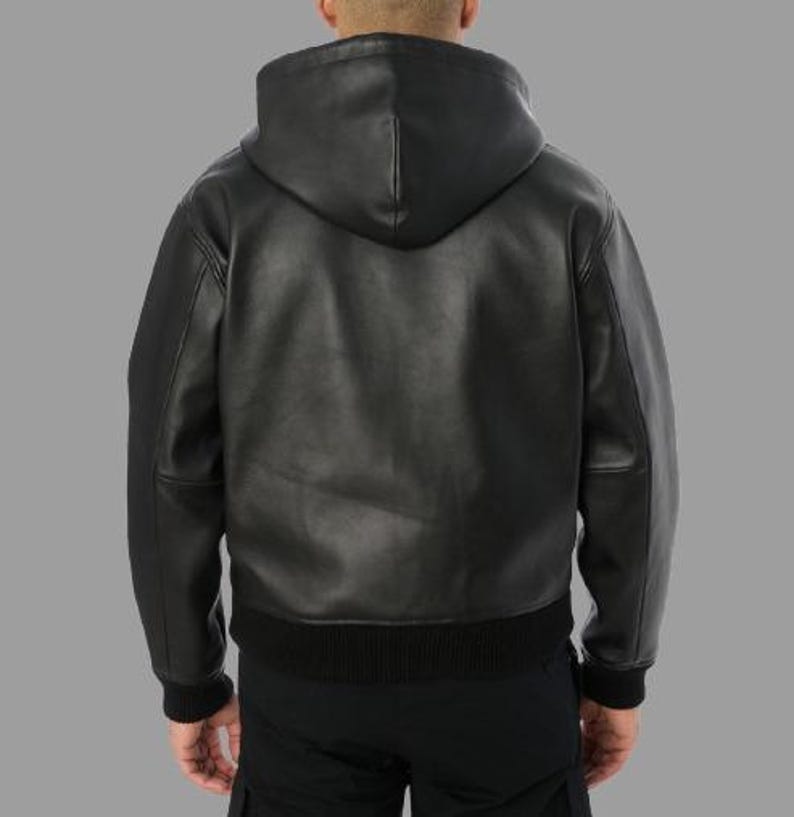 May include: Black leather hooded jacket with a ribbed hem and cuffs. The jacket has a full-length zipper and a hood. The model is wearing black pants. The jacket is made of a smooth, durable leather material.