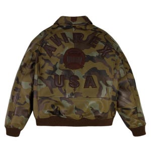 Puede incluir: Chaqueta bomber de camuflaje con ribete marr&oacute;n. La parte trasera de la chaqueta presenta el nombre de la marca "AVIREX" y "USA" en letras marrones. La chaqueta tiene un dise&ntilde;o cl&aacute;sico de chaqueta bomber.