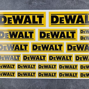 Könnte beinhalten: Ein Bogen mit gelben und schwarzen DEWALT Logo-Aufklebern in verschiedenen Größen. Die Aufkleber zeigen den Markennamen in fetten, schwarzen Großbuchstaben auf gelbem rechteckigem Hintergrund.