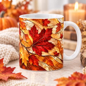 May include: A white ceramic mug featuring a vibrant, wrap-around print of autumn leaves in shades of deep red, burnt orange, and golden yellow. The design displays a dense pattern of maple and oak foliage with intricate vein details throughout.