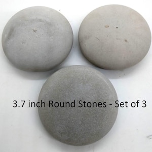 May include: Three round, gray stones with a textured surface. The stones are approximately 3.7 inches in diameter. The text on the image reads "3.7 inch Round Stones - Set of 3".