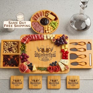 May include: A bamboo charcuterie board set featuring a central serving area with the engraved text Oktoberfest Oct 2026 The Weber, surrounded by compartments filled with meats, cheeses, grapes, nuts, and dried fruit, plus four matching coasters.