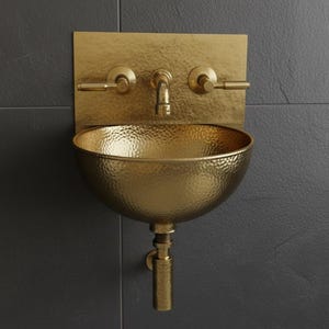May include: A hammered gold-colored wall-mounted sink with a matching faucet and handles. The sink has a rounded basin and is mounted on a dark gray tiled wall. The faucet and handles are horizontal.