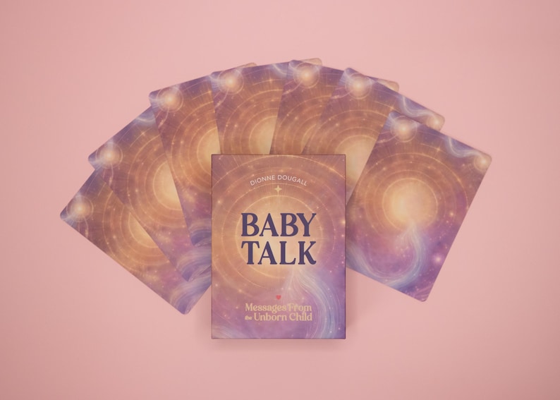 Puede incluir: Un mazo de cartas or&aacute;culo dispuesto en abanico detr&aacute;s de una caja central. Las cartas y la caja presentan un dise&ntilde;o c&oacute;smico en violeta y dorado con patrones de luz circulares. La caja muestra el texto BABY TALK y Messages from the Unborn Child de Dionne Douball.