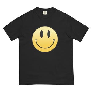 May include: Black t-shirt featuring a large, yellow smiley face graphic. The smiley face has black eyes and a curved smile. The t-shirt is made of a soft material and has a classic crew neck.