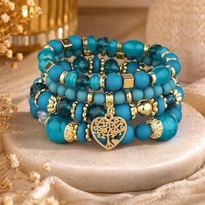 Peut inclure: Plusieurs bracelets empilés, composés de perles turquoise et bleu sarcelle avec des accents dorés. Les bracelets présentent diverses formes et tailles de perles, dont des perles rondes, à facettes et cubiques. Un bracelet a un charm en forme de cœur doré.