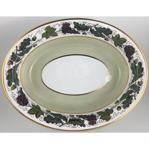 May include: Oval serving dish with a gold rim and a light green interior. The rim is decorated with a pattern of green leaves, purple grapes, and gold acorns. The center of the dish is white.