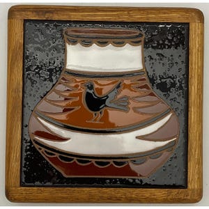 May include: A square ceramic tile framed in light brown wood featuring a glossy black background. Centered on the tile is a stylized brown vase with a white neck and base, decorated with a black bird graphic and scalloped edge details.