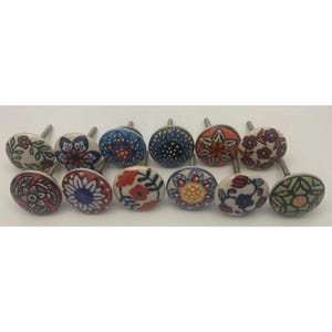 May include: A collection of twelve ceramic cabinet knobs with floral designs. Each knob features a different pattern in various colors, including red, blue, orange, and green, with silver-toned metal stems. The knobs are round and have a glossy finish.