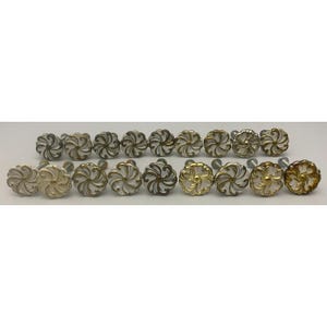 May include: A collection of eighteen round cabinet knobs arranged in two rows. Each knob features a white, swirling, floral-like pattern with metallic gold or bronze-toned accents on the edges and center, attached to a silver-colored metal bolt.