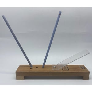 May include: A wooden knife sharpening guide with two angled, light blue sharpening rods. A clear plastic guide is attached to the wooden base. The text "HOLD HERE" is visible on the base.
