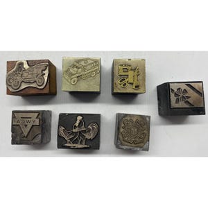 May include: A collection of seven rectangular printing blocks featuring various metal relief designs, including a vintage car, a truck, a sewing machine, a gift box, the YWCA logo, a rooster, and a circular emblem with an anchor and text.