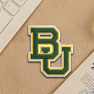 May include: A white ceramic mug with a black handle and the text "But First, Coffee" in a black, handwritten-style font. The mug is on a white surface.